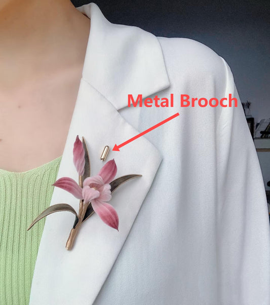 A close-up of a person wearing a white blazer with a beautiful handmade pink floral brooch affixed by a gold-tone metal lapel pin.