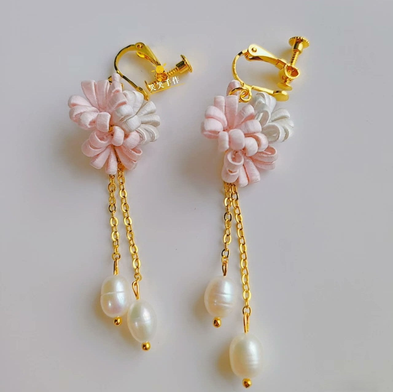 A pair of handmade pink and white Chanhua flower dangle earrings with natural freshwater pearls and gold 925 silver hooks on a white background.