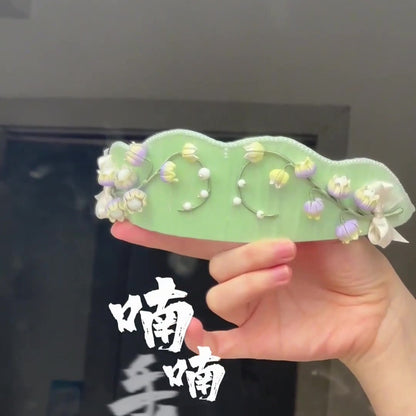 Artisanal floral crown showing intricate thread-wrapped blossoms and pearl accents on a soft green base.