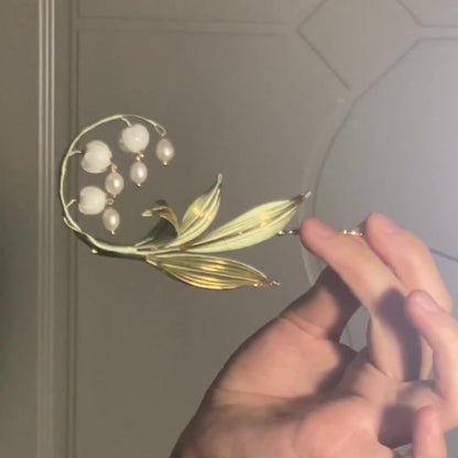 Hand holding a handmade Chanhua lily of the valley hair accessory against a neutral wall
