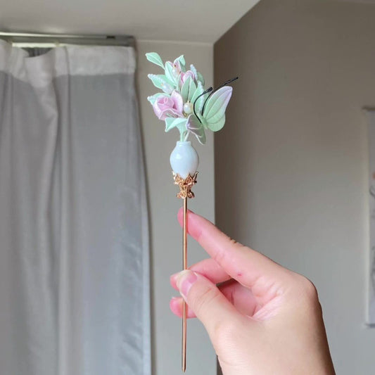 Hand holding a handmade Chanhua rose vase hair stick with pink roses and green butterfly details