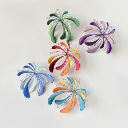 A flat lay of five colorful, firework-shaped DIY Chanhua hairpins or brooches in green, purple, red, blue, and orange, arranged on a white background.