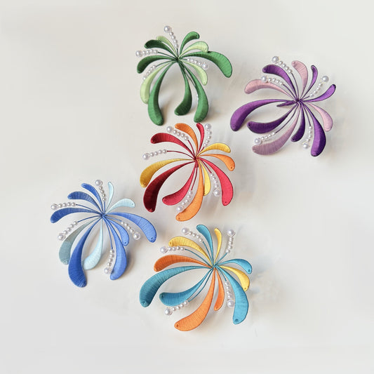 A flat lay of five colorful, firework-shaped DIY Chanhua hairpins or brooches in green, purple, red, blue, and orange, arranged on a white background.