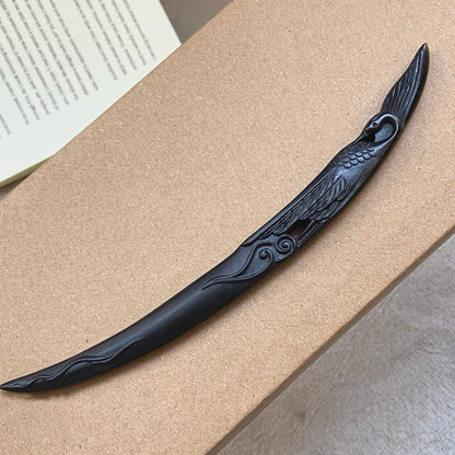 Natural African Blackwood hair stick with crane and moon design 18cm on wooden surface with book background.