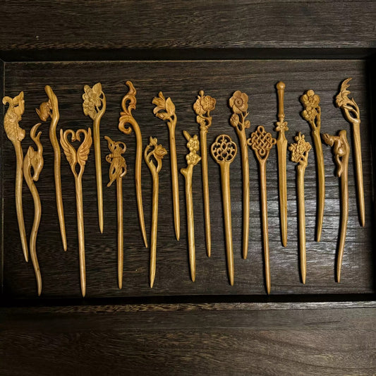 Set of natural peach wood hair sticks with assorted floral, bird, and nature carvings displayed in wooden tray