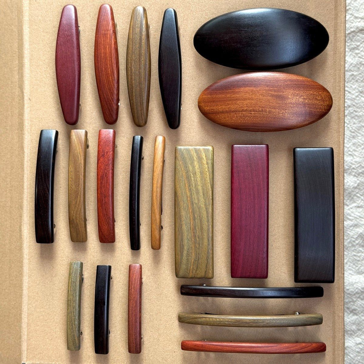 Collection of natural African blackwood and red sandalwood hair clips in assorted shapes and colors displayed on neutral background