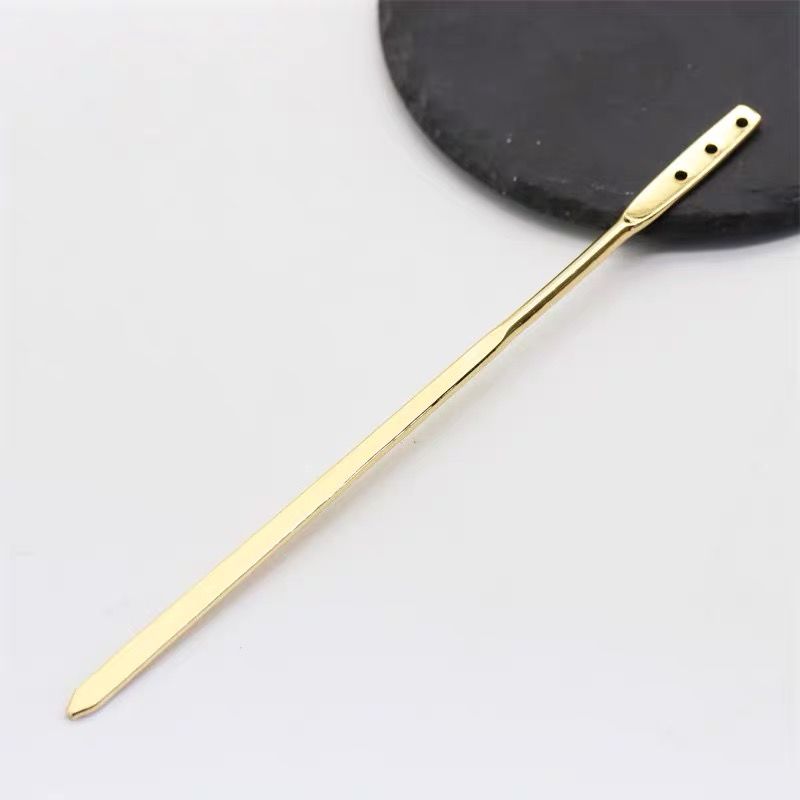 Close-up of the perforated end of a gold metal hairpin base, showing detail for attaching charms.