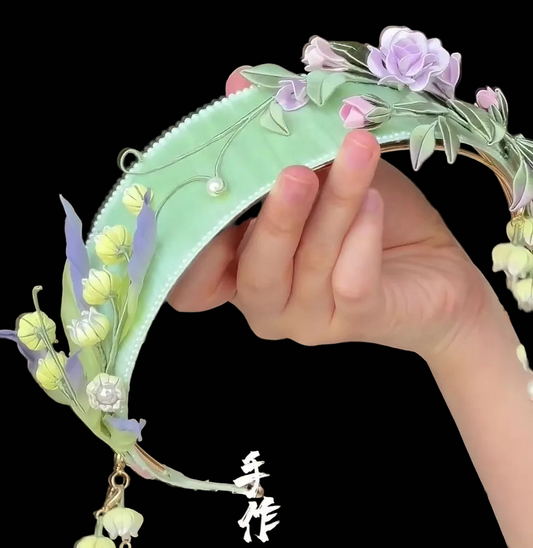 Handcrafted Chanhua headband featuring purple thread-wrapped roses and pale yellow Lily of the Valley flowers on a light green base.