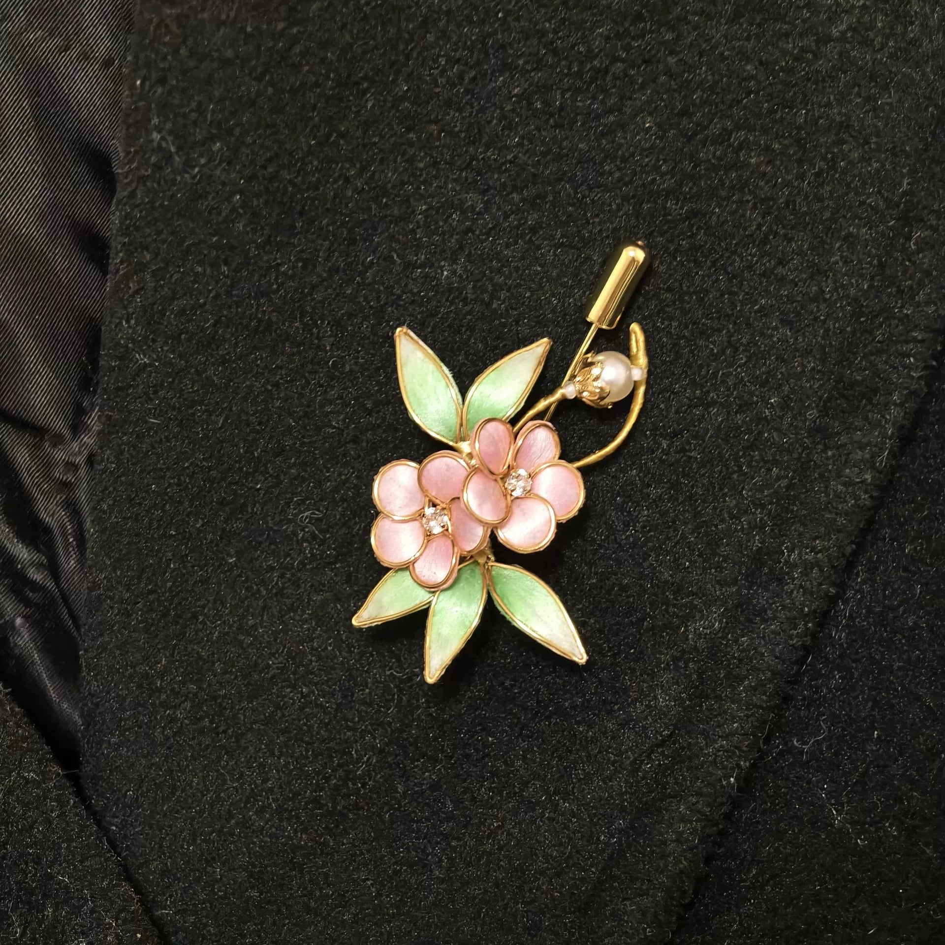 Handmade Ronghua brooch featuring two pink silk velvet flowers with gold-toned edges, light green leaves, and a pearl accent pinned on black fabric.