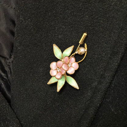 Handmade Ronghua brooch featuring two pink silk velvet flowers with gold-toned edges, light green leaves, and a pearl accent pinned on black fabric.