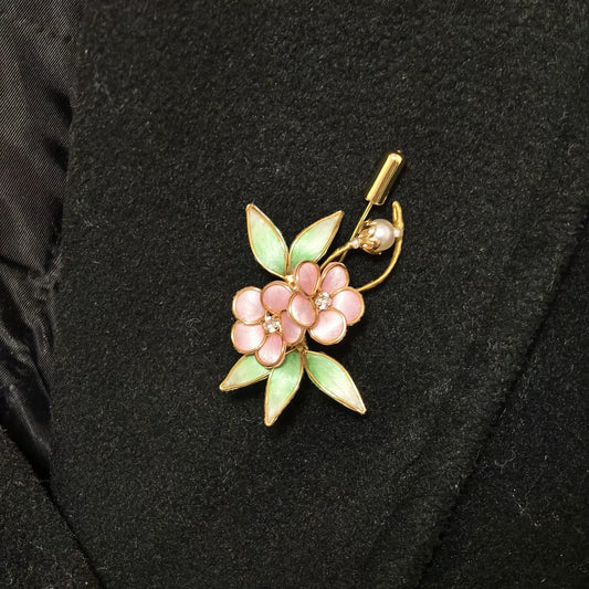 Handmade Ronghua brooch featuring two pink silk velvet flowers with gold-toned edges, light green leaves, and a pearl accent pinned on black fabric.