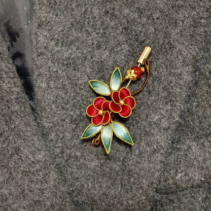 Handmade Ronghua brooch featuring two red silk velvet flowers with gold-toned edges, gradient green leaves, and a red bead accent pinned on grey fabric.