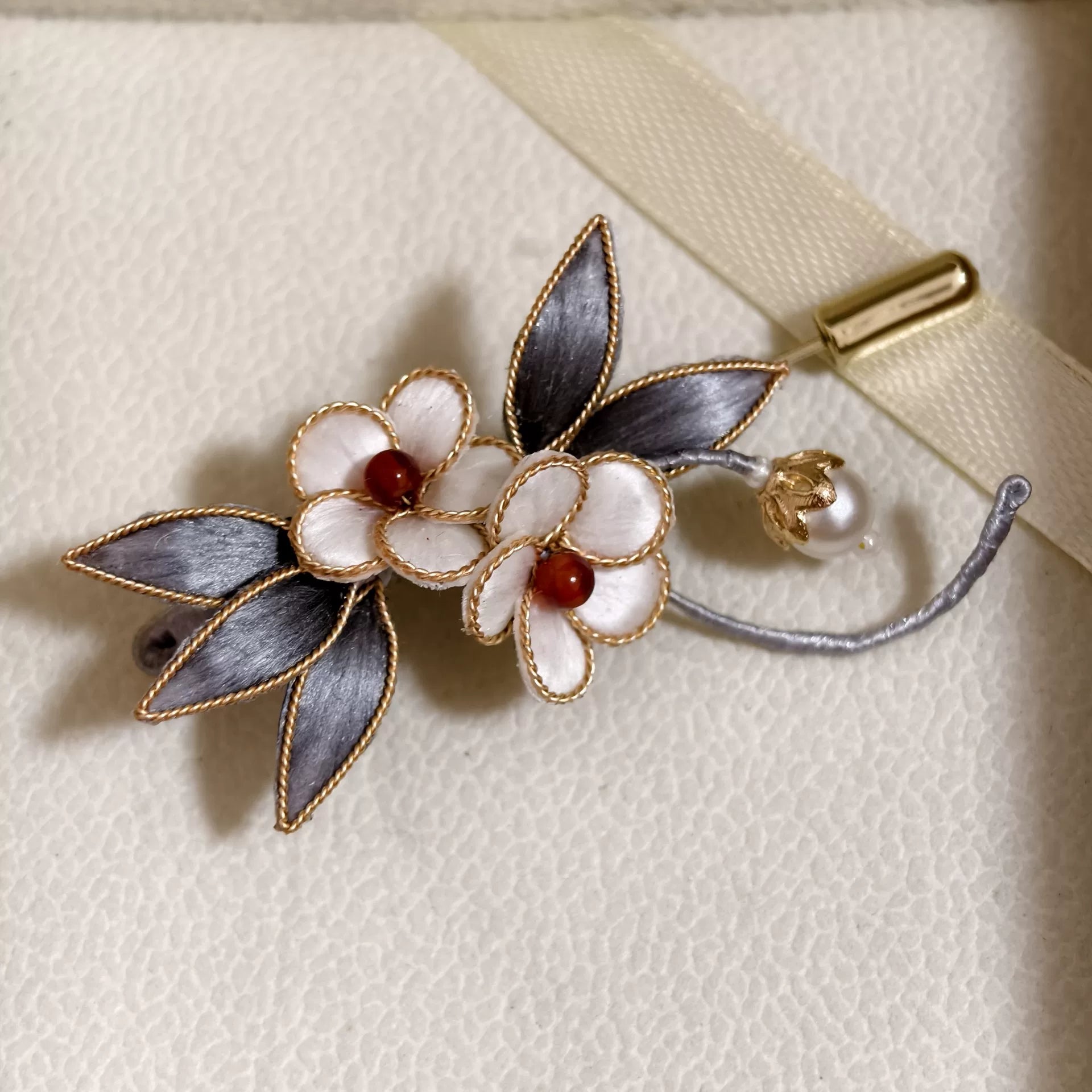 Handmade Ronghua brooch featuring two white silk velvet flowers with gold-toned edges, dark silver-grey leaves, and a hanging pearl accent on a gold pin.