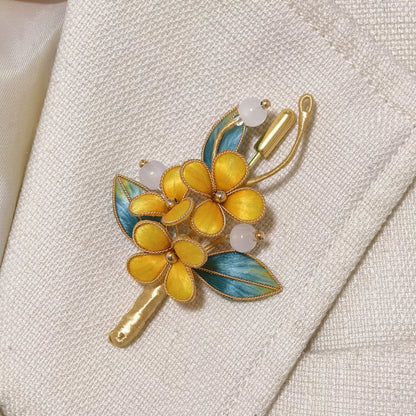 Handmade Ronghua brooch featuring three vibrant yellow silk velvet flowers with gold-toned edges, teal-green leaves, and white beads pinned on textured off-white fabric.