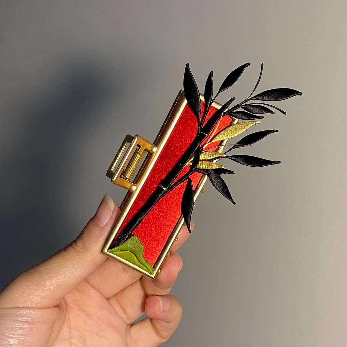 Hand holding a handmade Chanhua bamboo leaf hair clip against a plain gray background