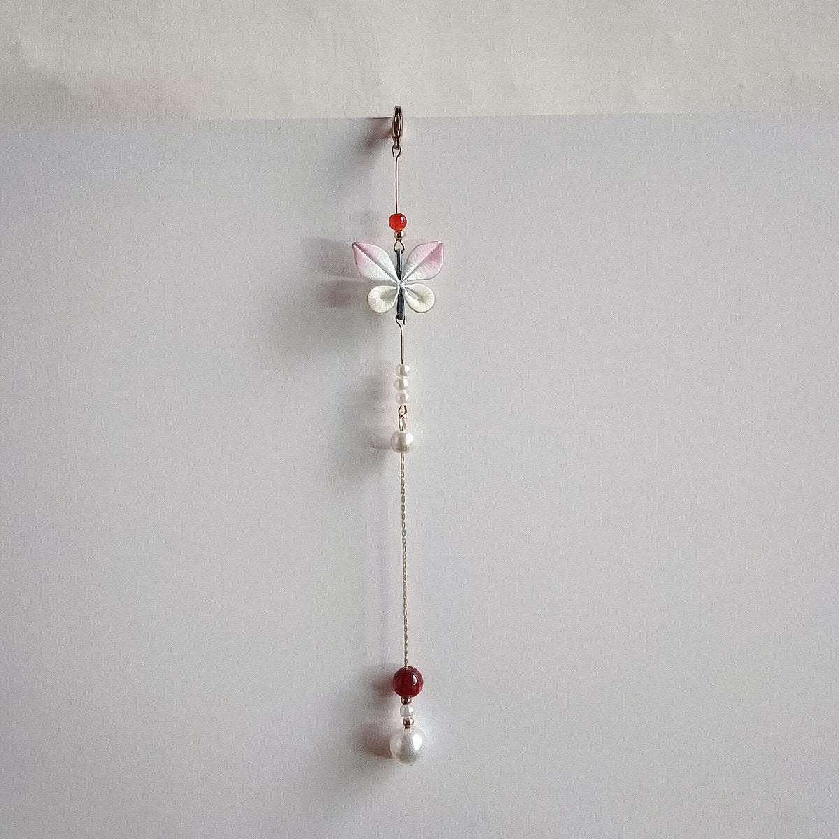 Handcrafted Chanhua thread-wrapped butterfly pendant with pink and white wings and a long gold chain tassel featuring pearl and red bead accents.