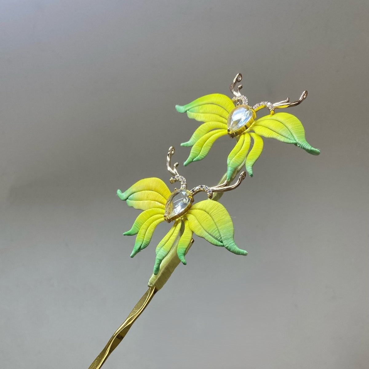 Handmade Chanhua deer floral hair pin with gradient yellow-green petals and crystal accents on a plain gray background