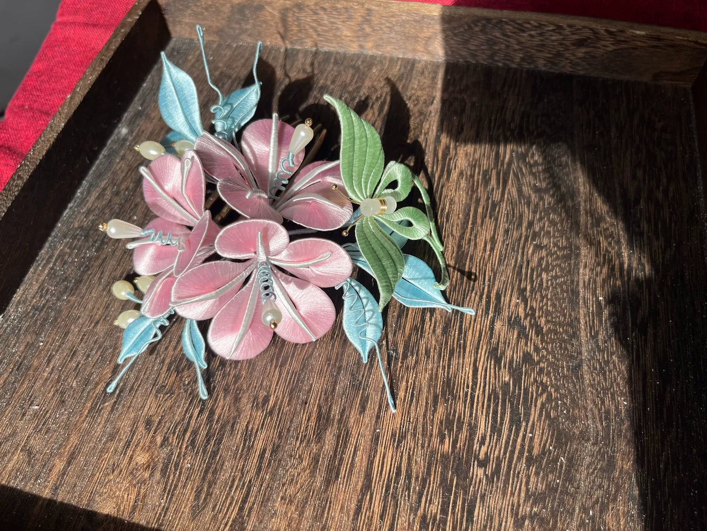 A handmade Chanhua morning glory hairpin with pink flowers and blue - green leaves on a wooden tray