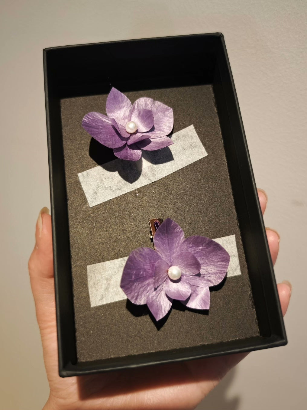 Handheld black box containing two purple Ronghua phalaenopsis hair accessories/brooches with pearl centers
