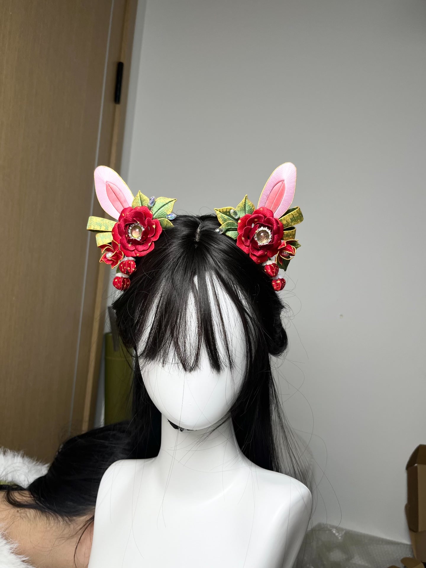 A pair of handmade Chanhua Christmas - style bunny - ear hair clips with red flowers and green leaves, on a mannequin's head