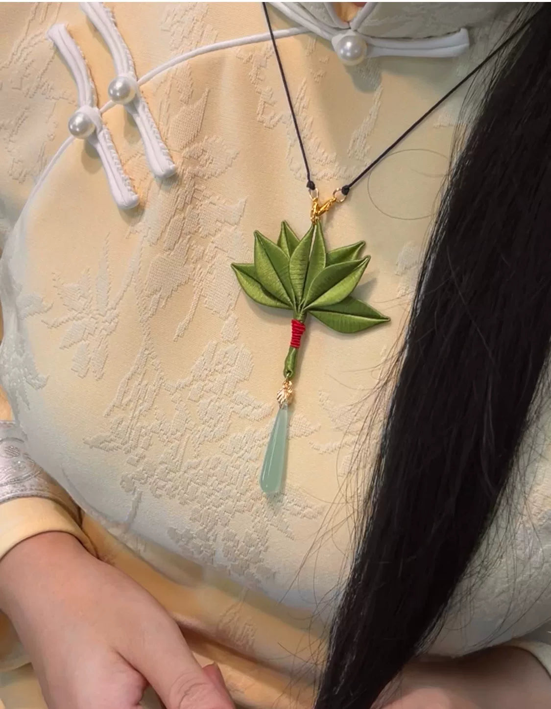A handmade Chanhua pomelo - leaf necklace with a green leaf pendant, red - wrapped base, and light green teardrop charm worn on a yellow traditional garment