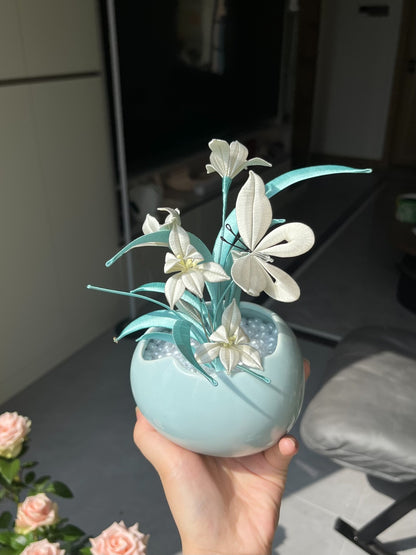 A black graduation cap adorned with white handmade Chanhua and turquoise - colored leaves, held by a hand-4