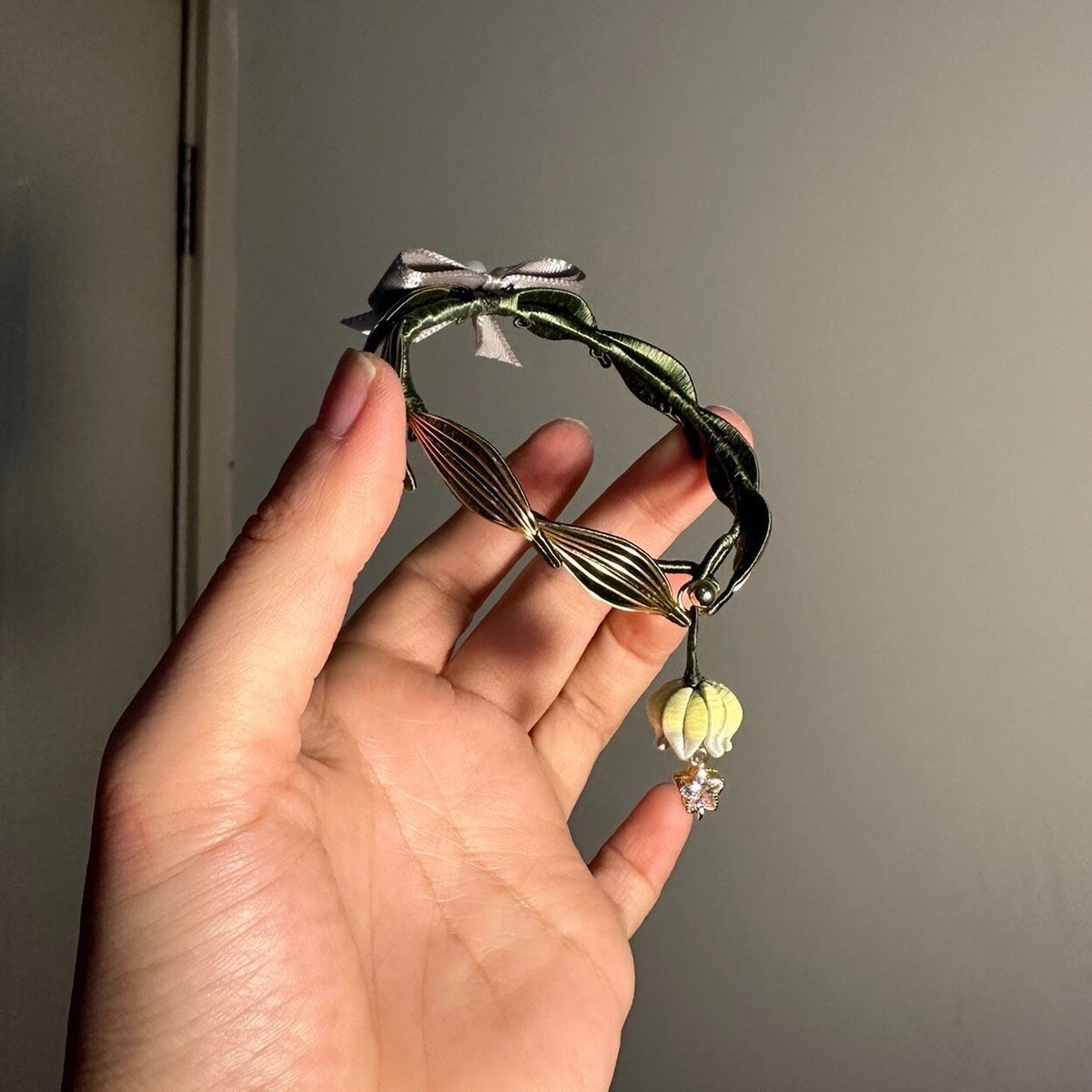 Human hand holding a finished handmade Chanhua lily of the valley bracelet against a plain grey background