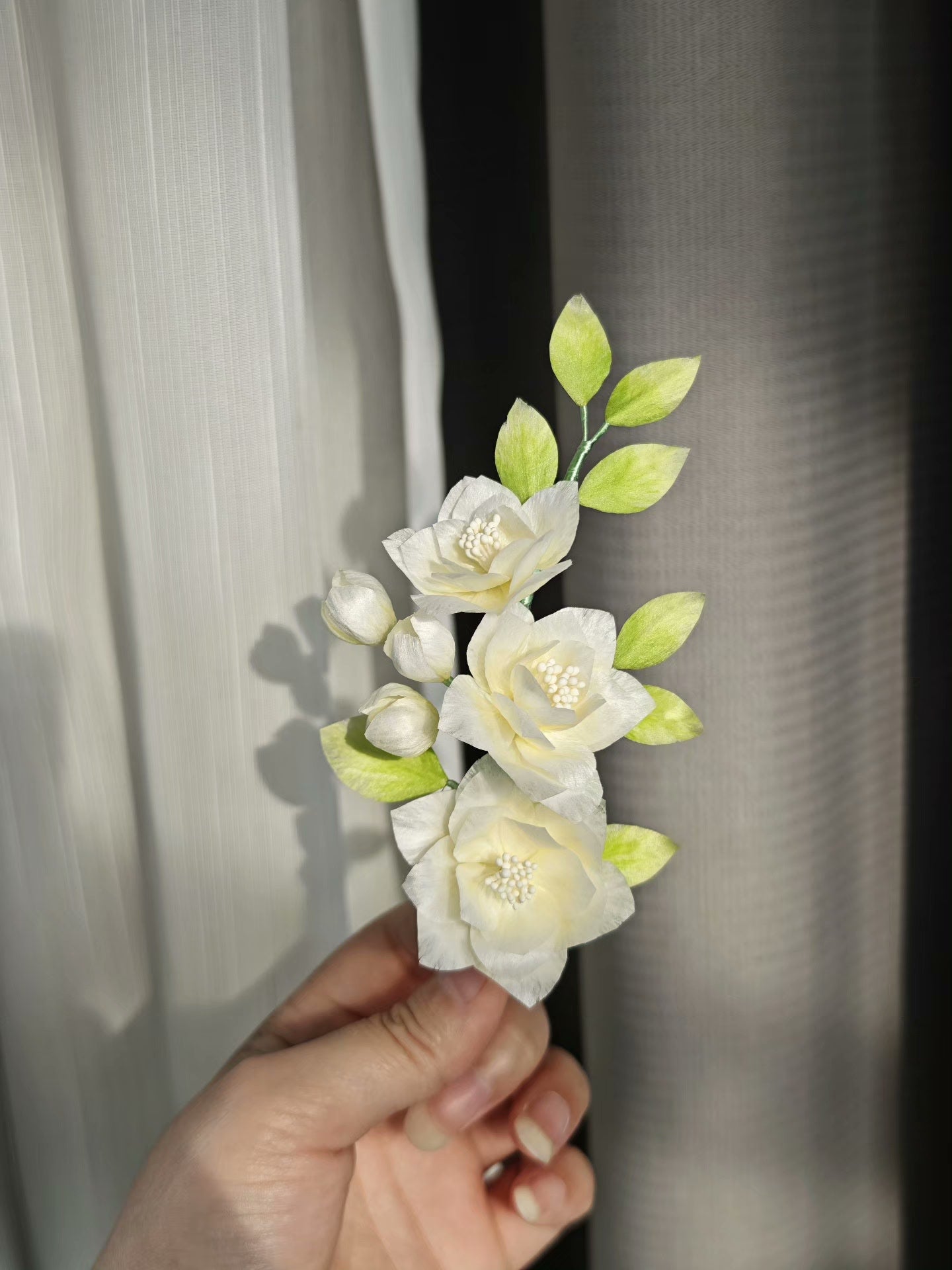 A hand - held handmade Ronghua jasmine flower hair accessory with white flowers and green leaves