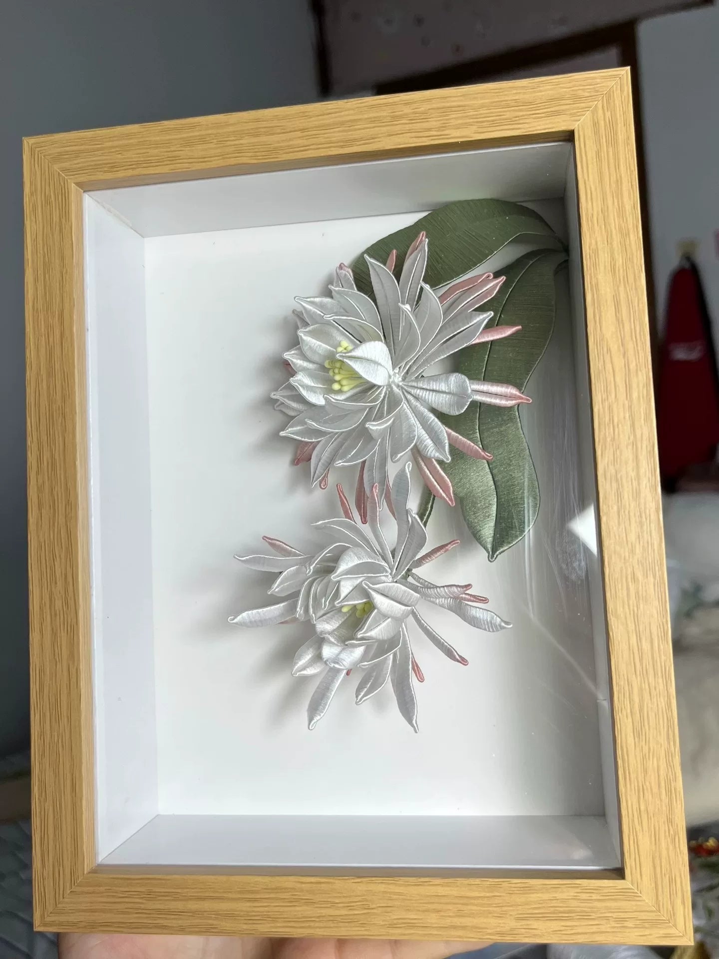 A handmade Chanhua table display in a wooden box with white and pink petals and green leaves