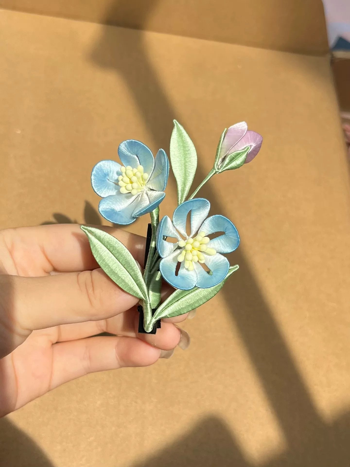 A hand - made Chanhua hair clip with blue flowers, green leaves and a budding flower