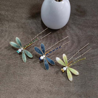 Ronghua handmade dragonfly hairpins in three colors — blue, mint green, and yellow-green — with shimmering silk wings and beaded bodies, displayed on a grey fabric background beside a white ceramic vase