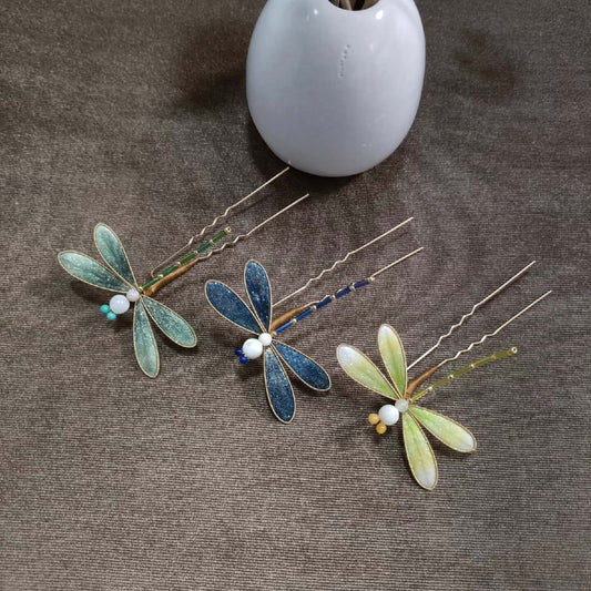 Ronghua handmade dragonfly hairpins in three colors — blue, mint green, and yellow-green — with shimmering silk wings and beaded bodies, displayed on a grey fabric background beside a white ceramic vase