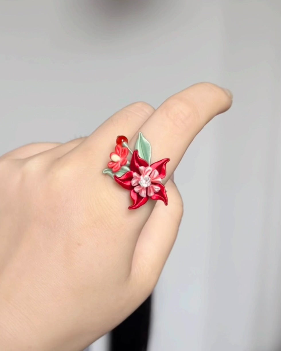 A hand wearing a vibrant red Handmade Chanhua Mandala Ring with green leaves and pink details