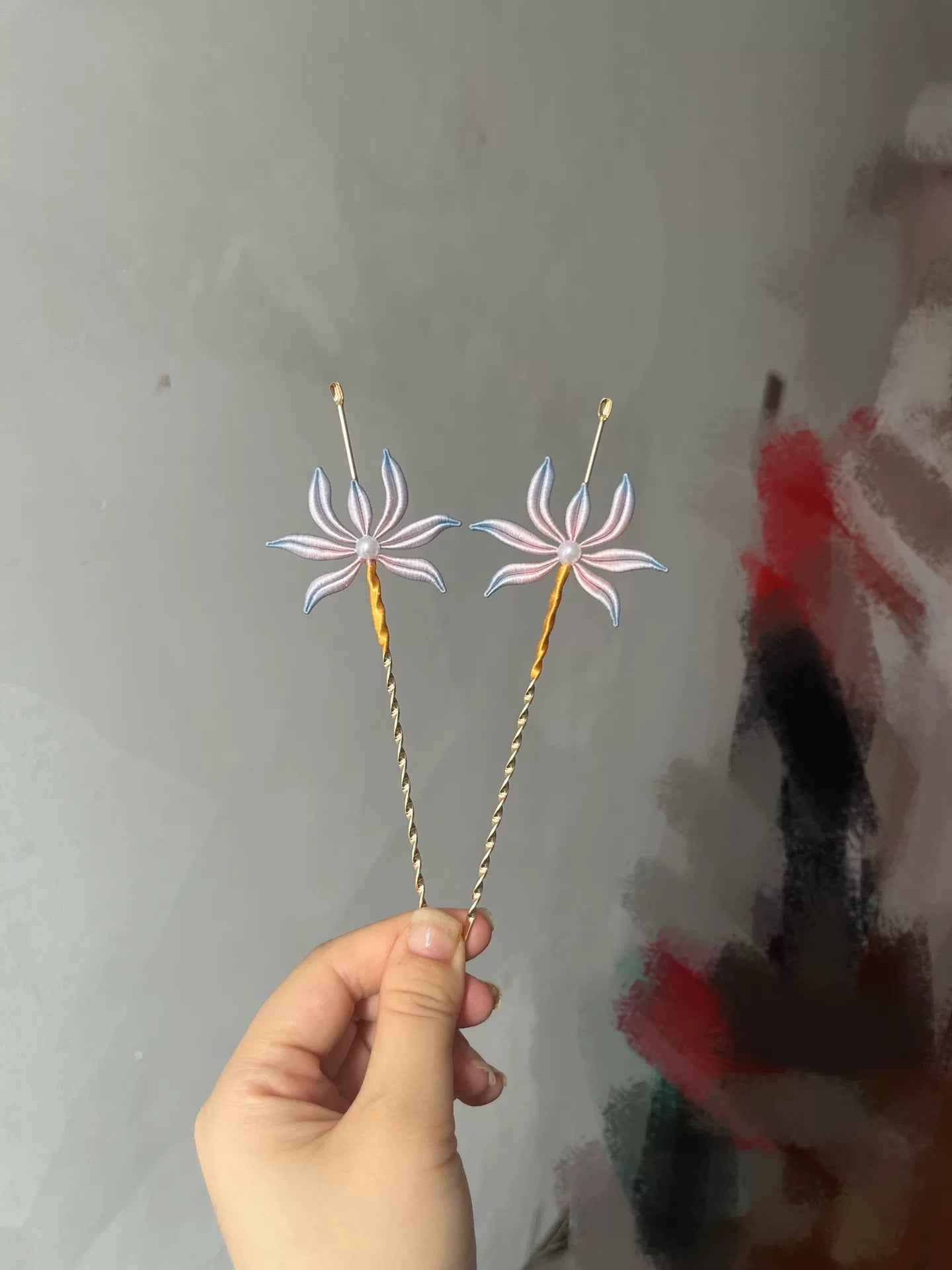 Two handmade Chanhua orchid - patterned ear - pick hairpins held by a hand
