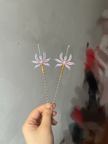Two handmade Chanhua orchid - patterned ear - pick hairpins held by a hand