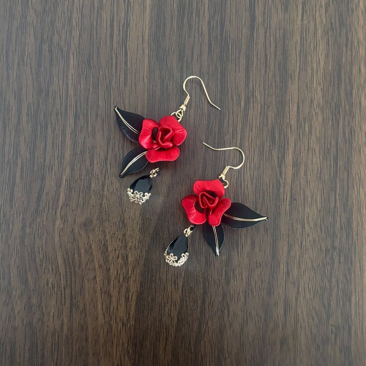 Handcrafted Chanhua thread-wrapped earrings featuring a blooming red rose with black leaves and black teardrop dangles on a wooden background.