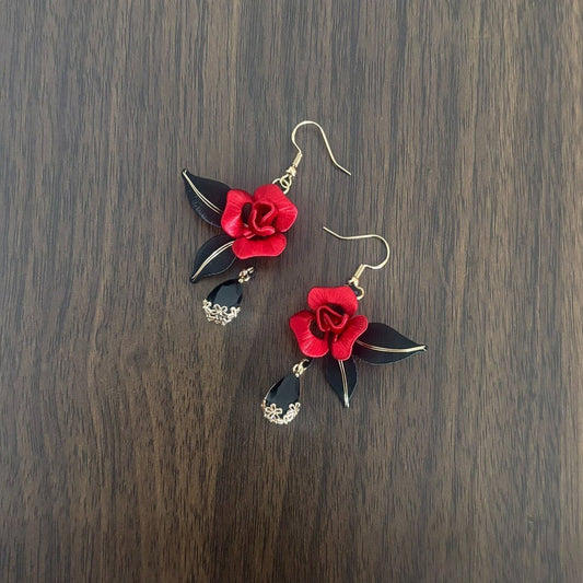 Handcrafted Chanhua thread-wrapped earrings featuring a blooming red rose with black leaves and black teardrop dangles on a wooden background.