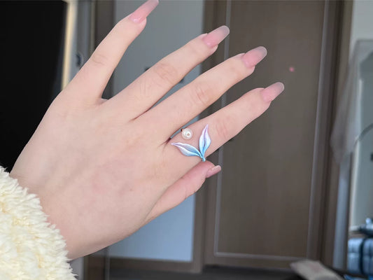 A hand wearing a blue mermaid tail ring and holding a blue mermaid tail necklace-2