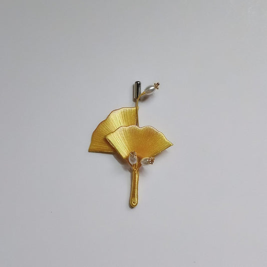A traditional Chinese thread-wrapped (Chanhua) golden ginkgo leaf pin on a plain background, showing artisanal 3D textures.