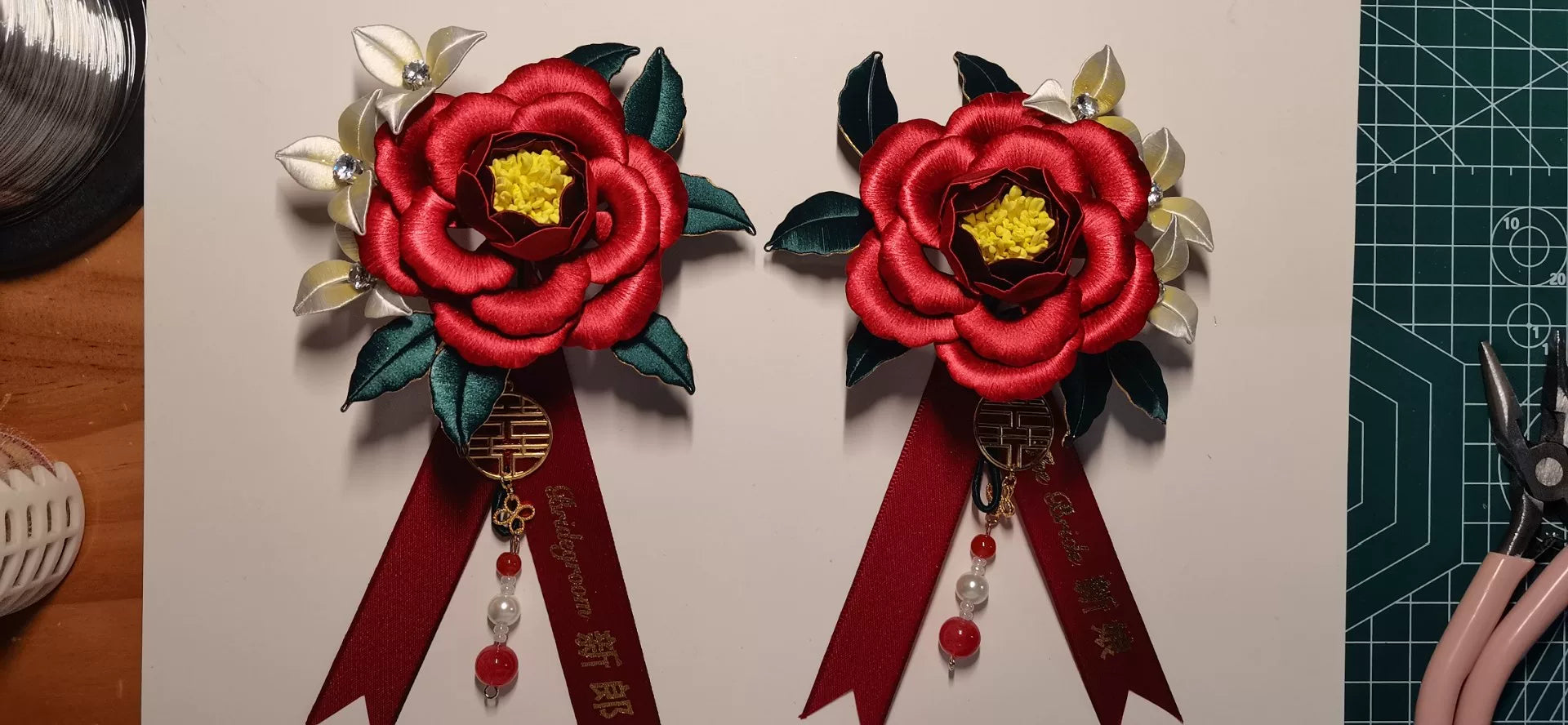 Two red handmade Chanhua bridal boutonnieres with customizable ribbons on a red background-2