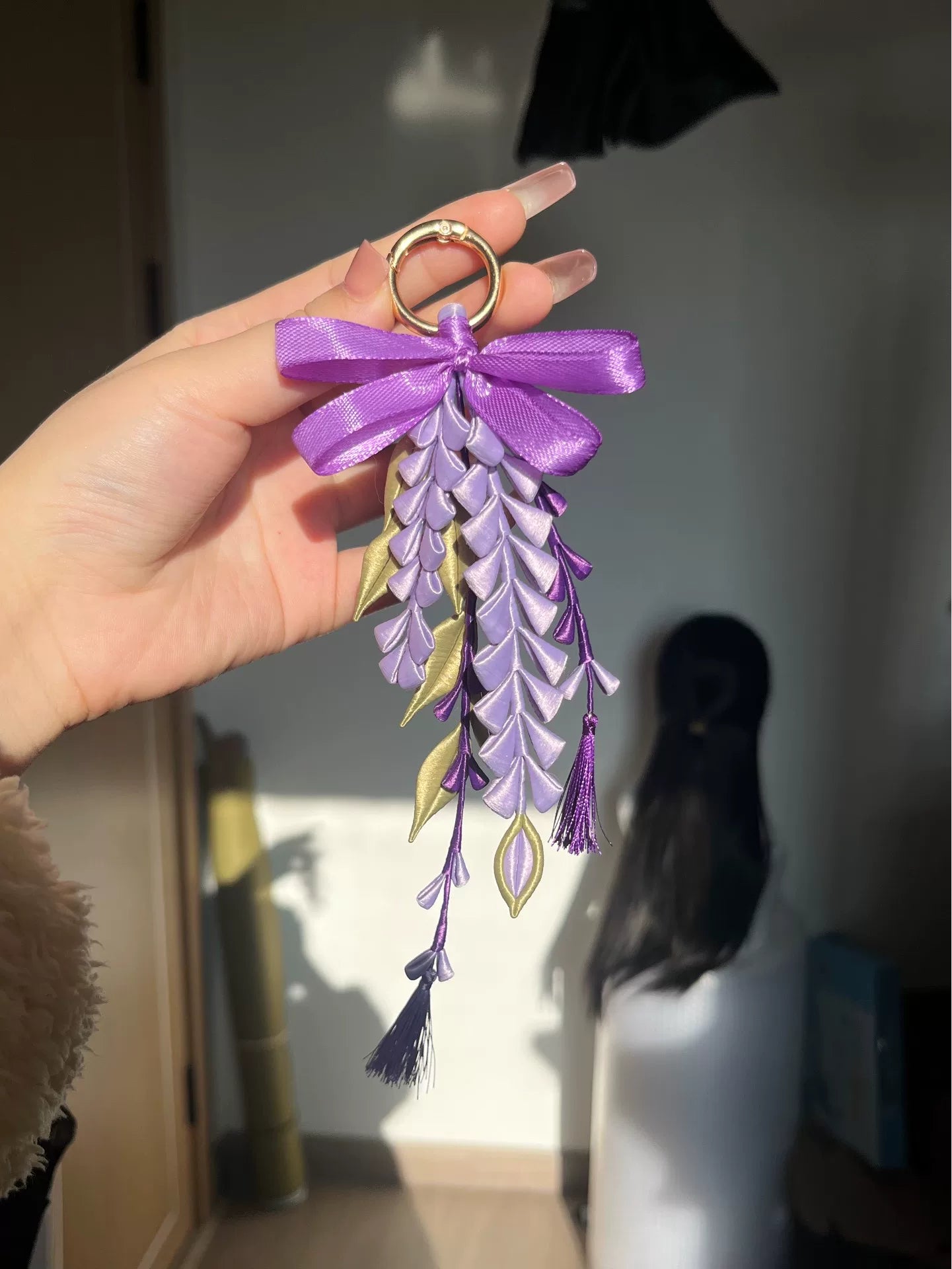 A hand - held purple wisteria keychain with a golden ring and decorative bow