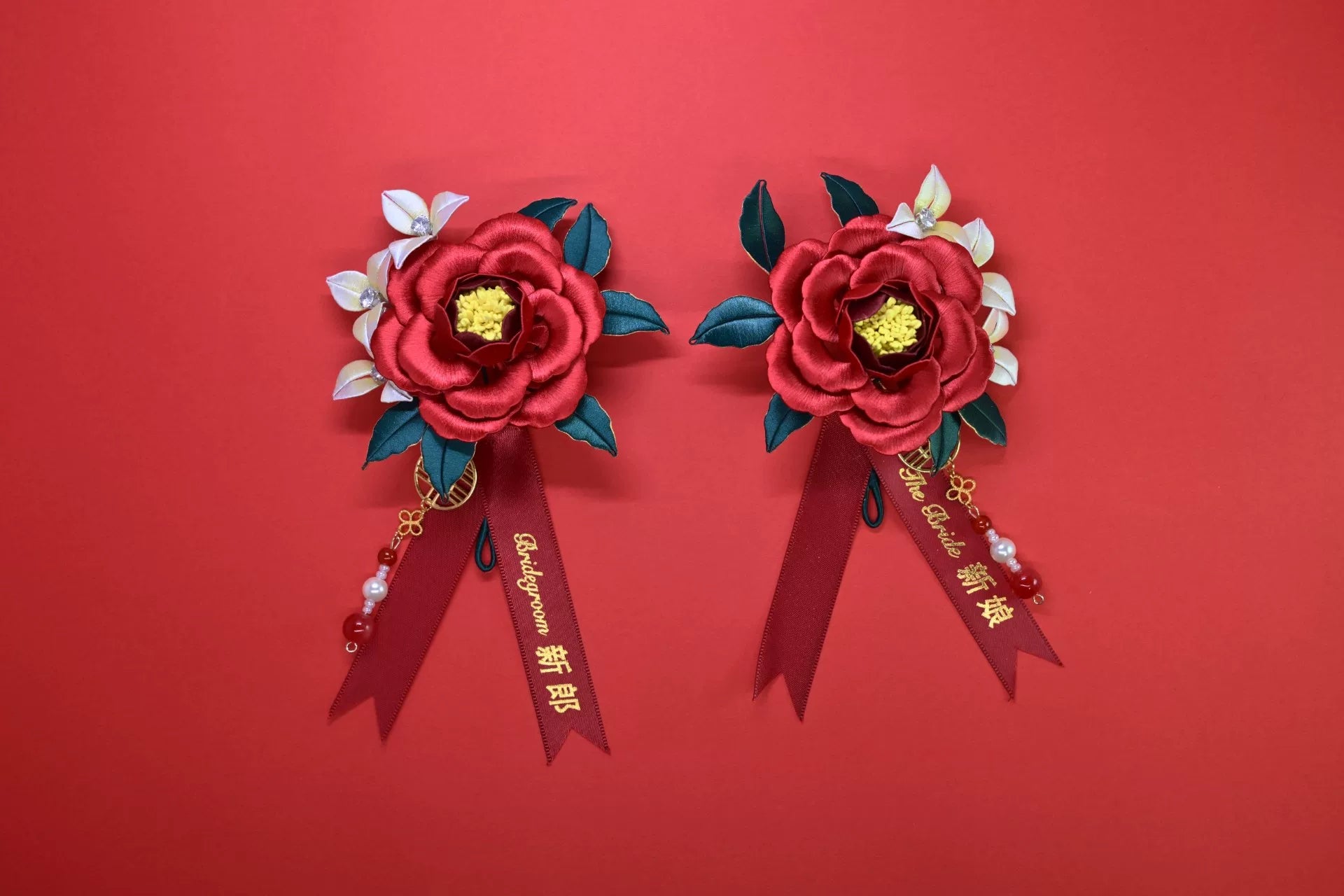Two red handmade Chanhua bridal boutonnieres with customizable ribbons on a red background
