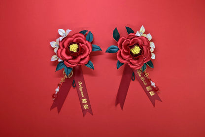 Two red handmade Chanhua bridal boutonnieres with customizable ribbons on a red background
