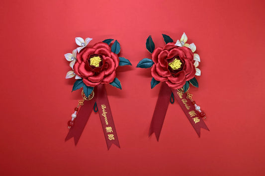 Two red handmade Chanhua bridal boutonnieres with customizable ribbons on a red background