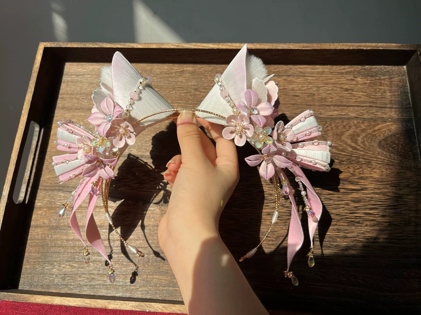 A hand - held handmade Chanhua cat - ear hair hoop with pink and white floral and beaded decorations