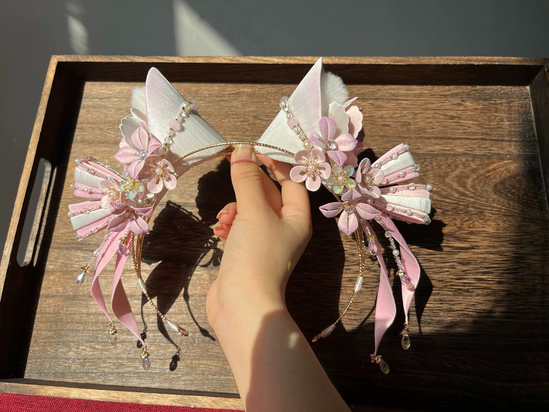 A hand - held handmade Chanhua cat - ear hair hoop with pink and white floral and beaded decorations