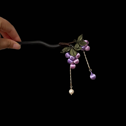 Handheld view of a handcrafted Chanhua thread-wrapped hairpin featuring a cluster of purple grapes, green leaves, and pearl tassel drops.
