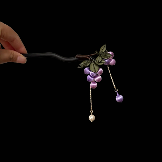 Handheld view of a handcrafted Chanhua thread-wrapped hairpin featuring a cluster of purple grapes, green leaves, and pearl tassel drops.