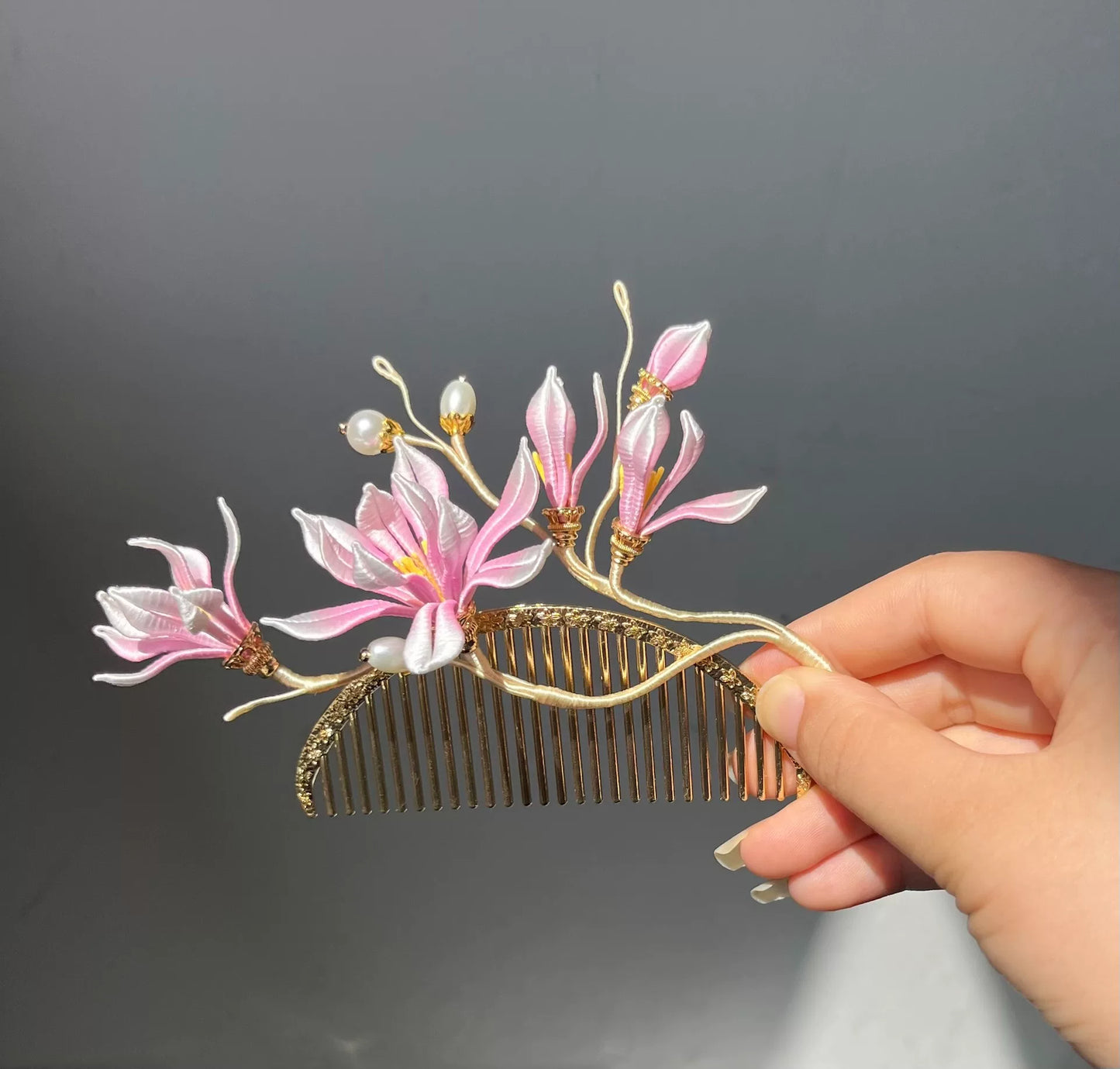 A hand - held golden hair comb with pink handmade Chanhua magnolia flowers and pearls