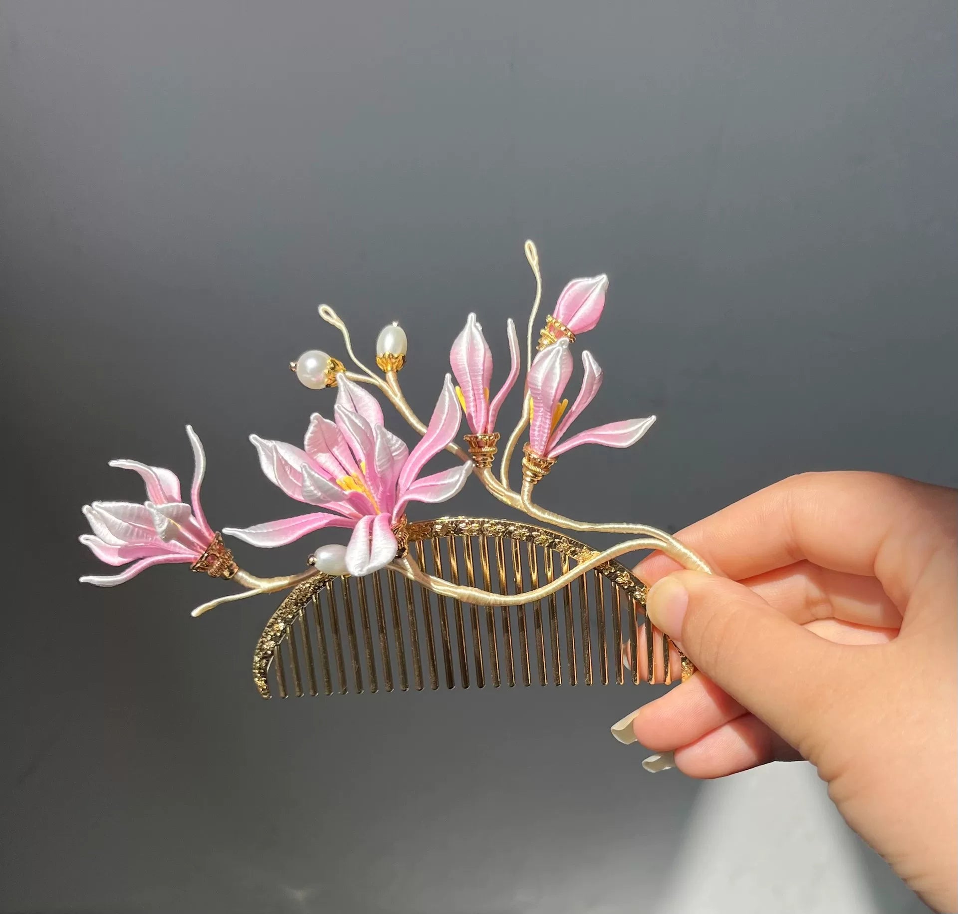 A hand - held golden hair comb with pink handmade Chanhua magnolia flowers and pearls